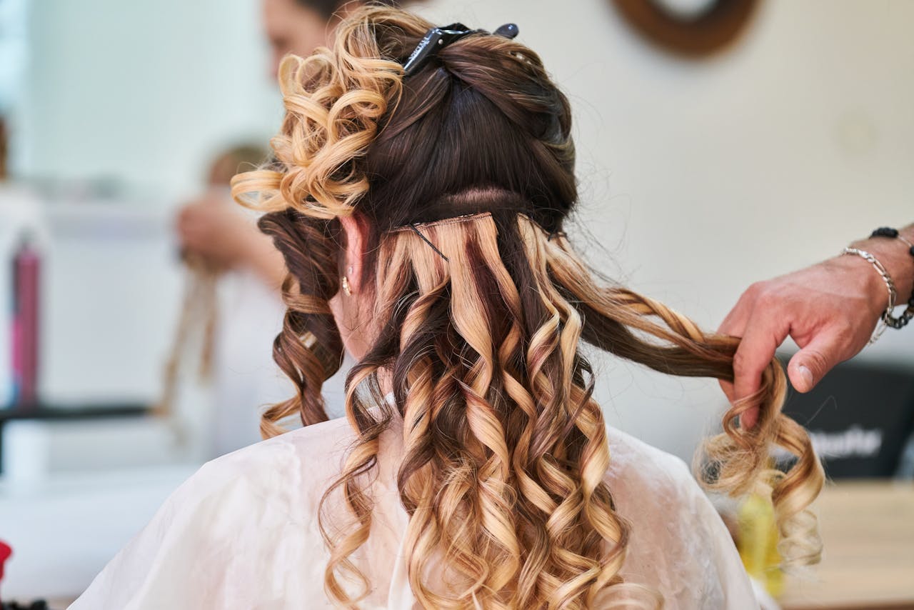 gallery-3 Close-up of hairstylist perfecting curls on a woman's hair in a salon setting.