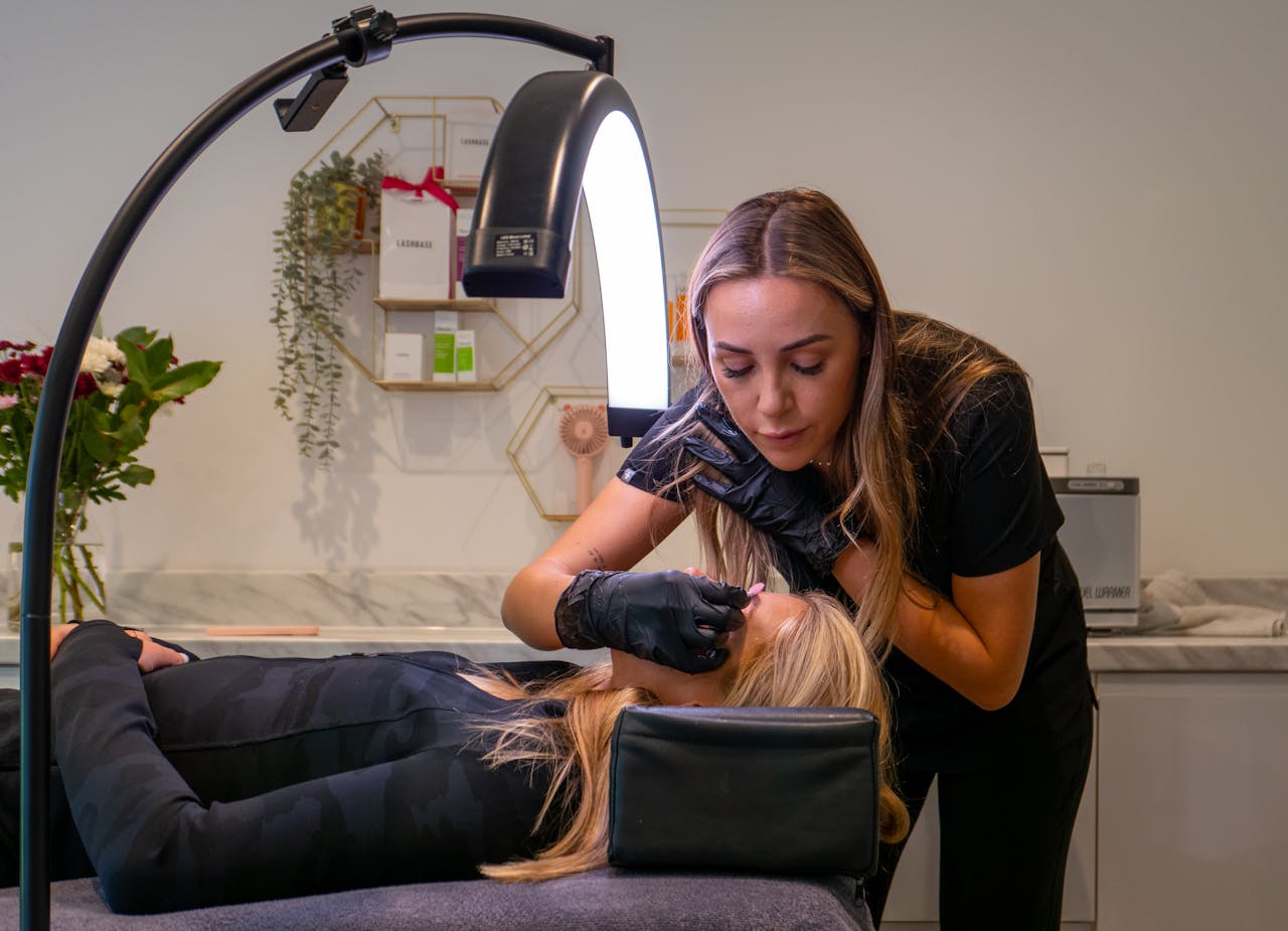 contact-img Beauty technician applying eyelash extensions to a client in a modern salon setting.